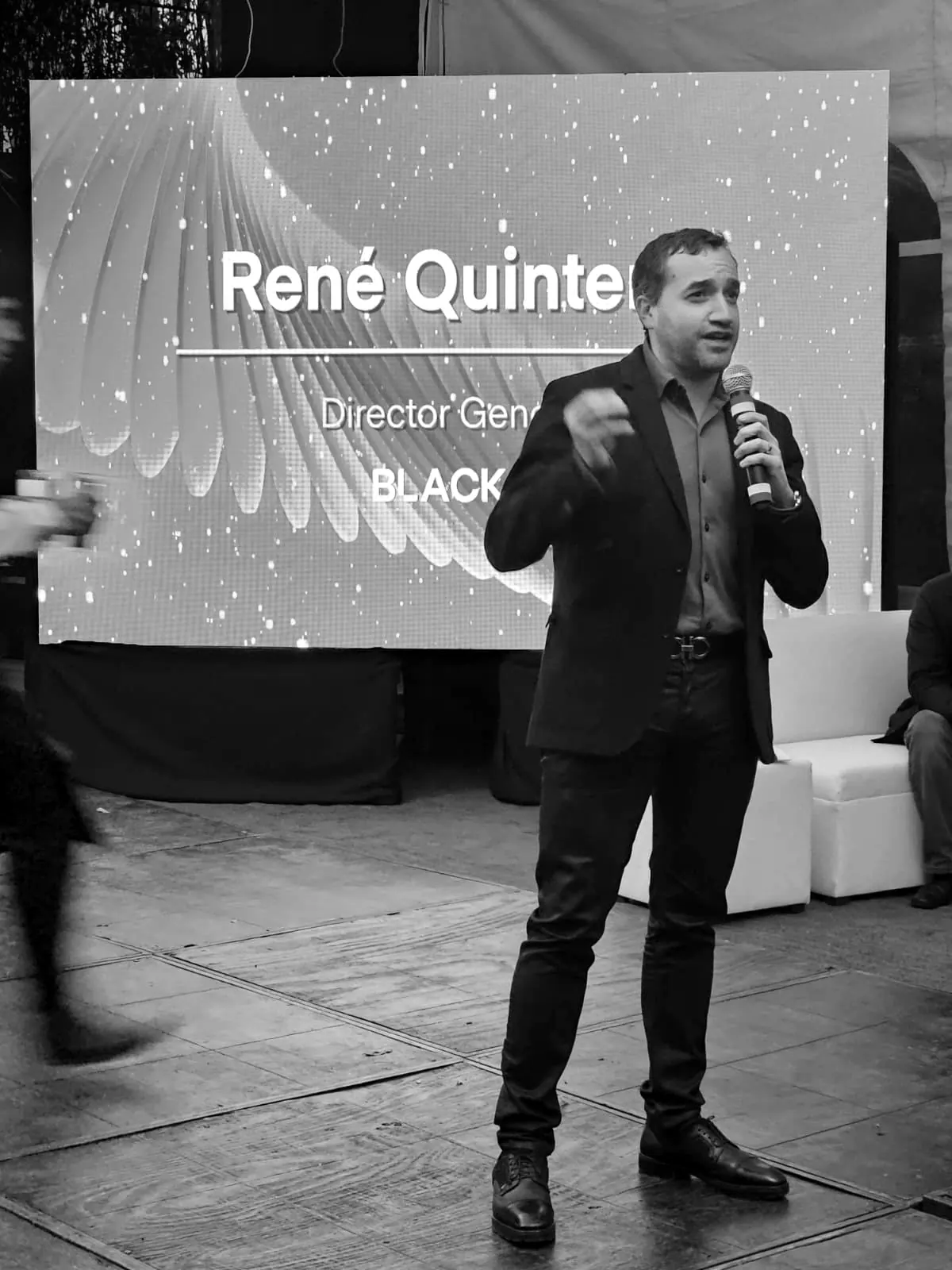 René Quintero hablando con micrófono frente a una pantalla con su nombre